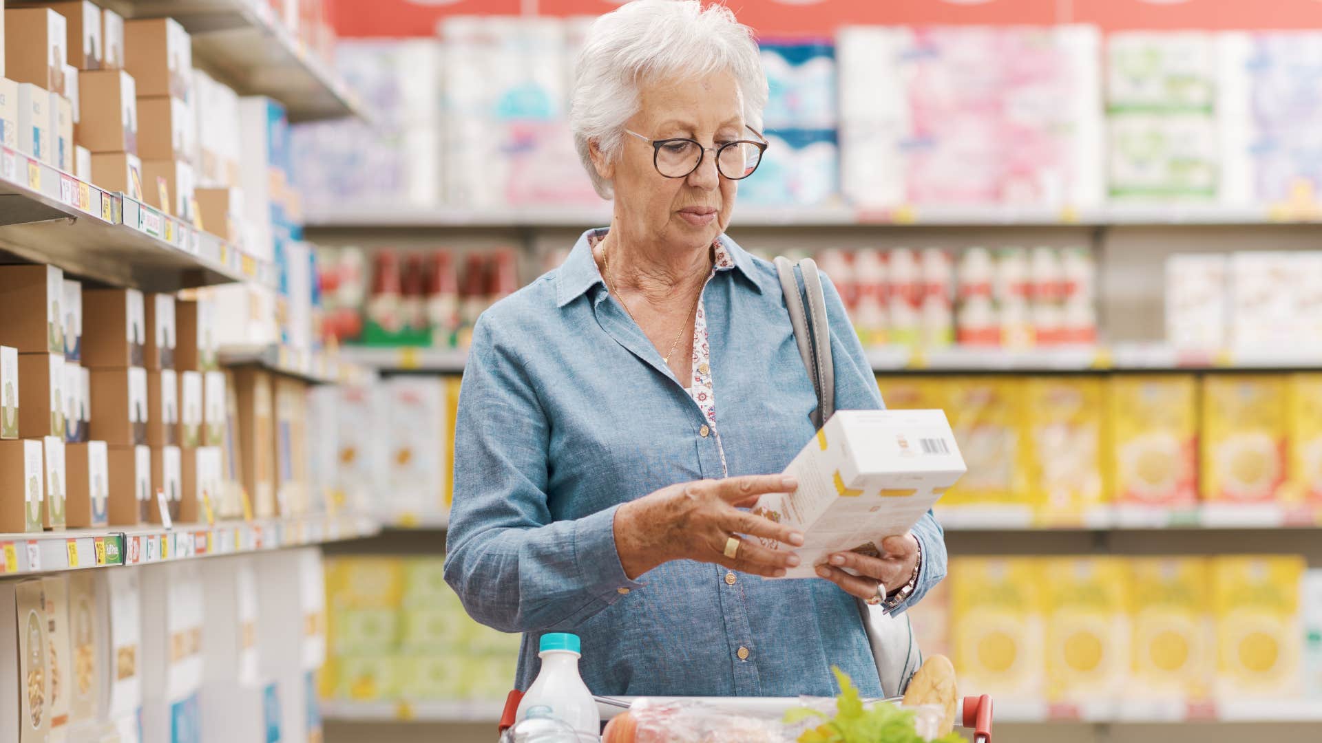 Older woman looking at a box in a grocery store aisle