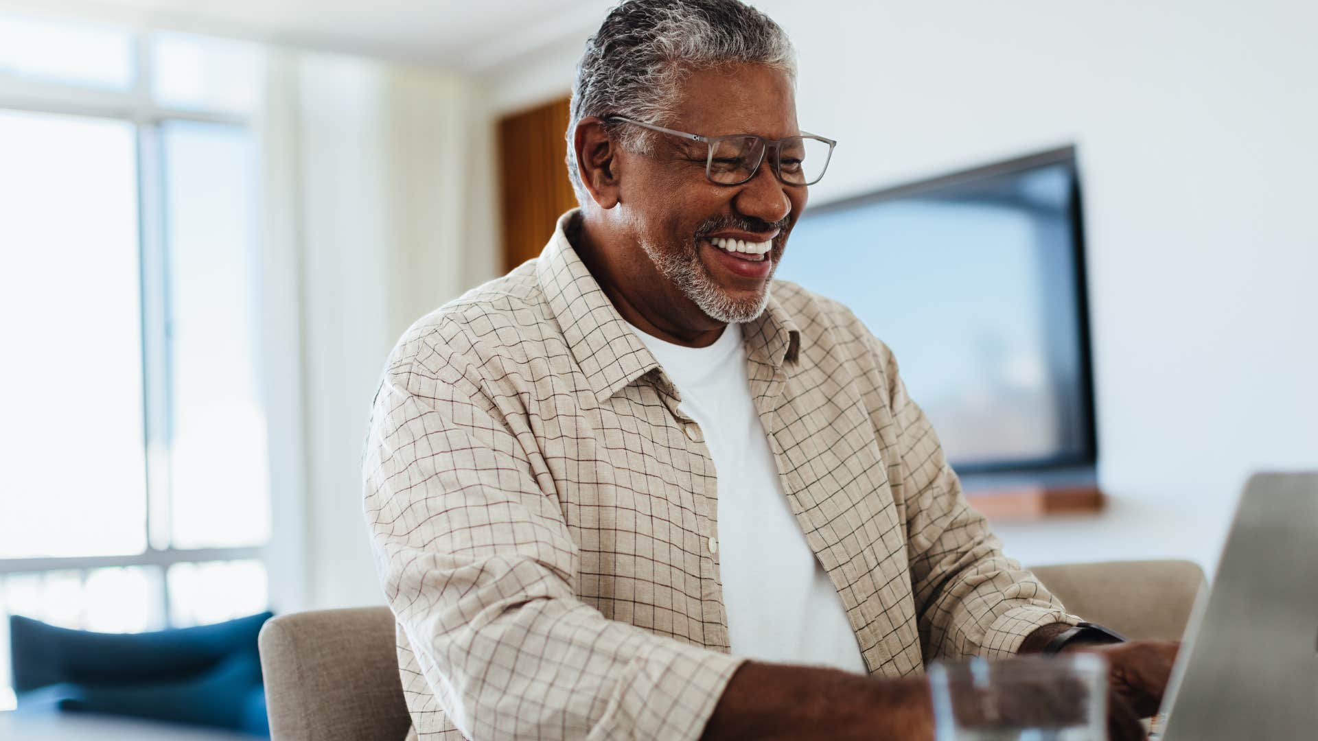 Older man smiling and typing on his laptop