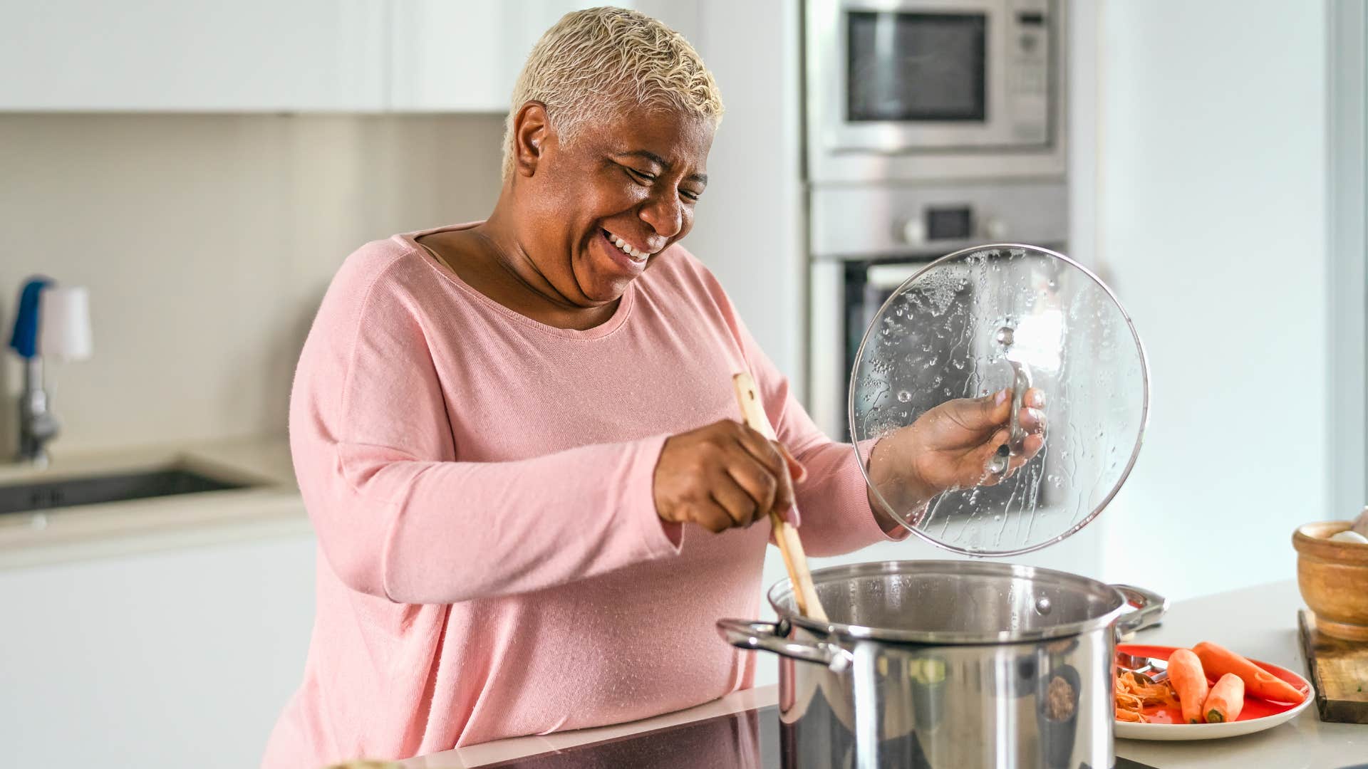 Older woman smiling and stirring a pot on the stove.