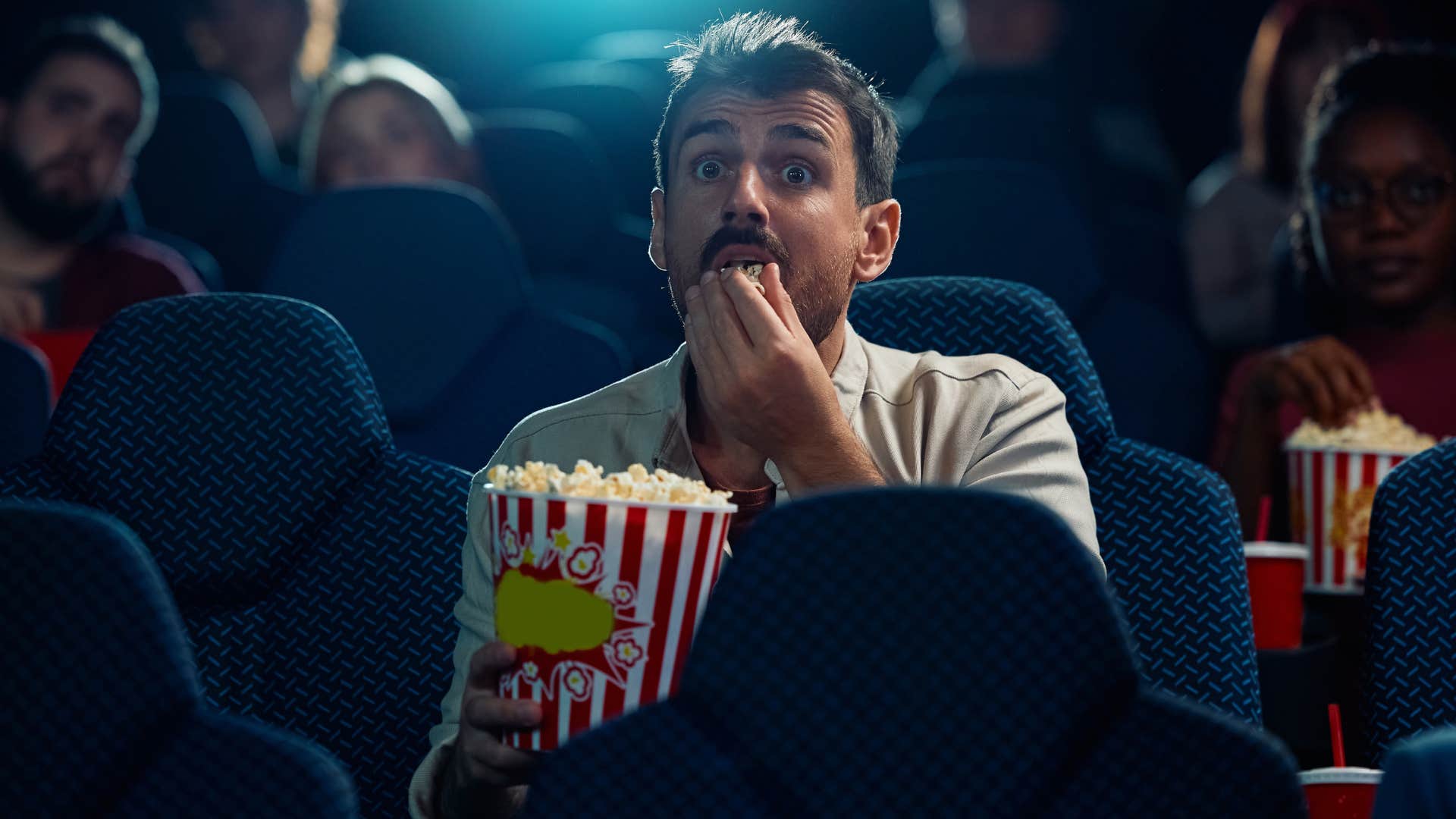 Man looking scared eating popcorn in a movie theater