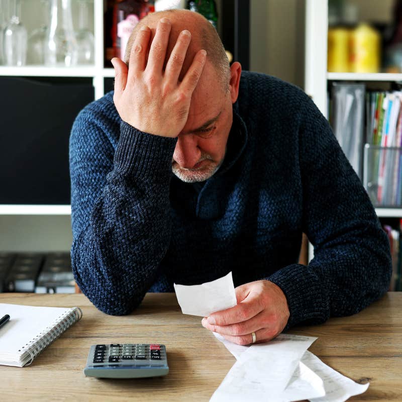 man holding his head while doing finances at table