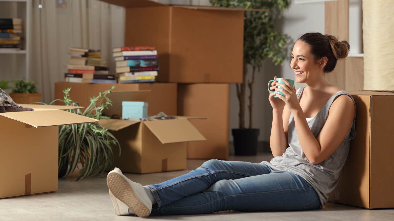 Happy tenant resting drinking coffee moving home sitting on the floor in the night