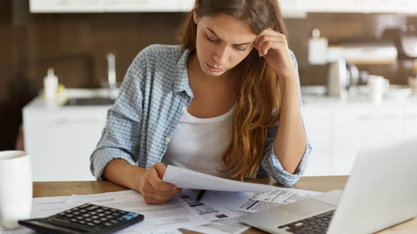 young woman with calculator, computer and bills spread out across table