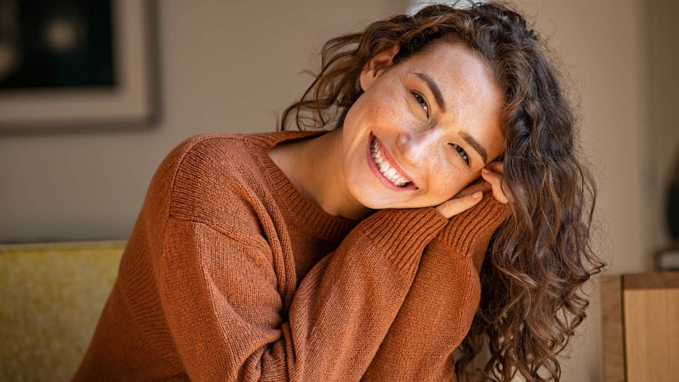 Happy young woman sitting on sofa at home and looking at camera.