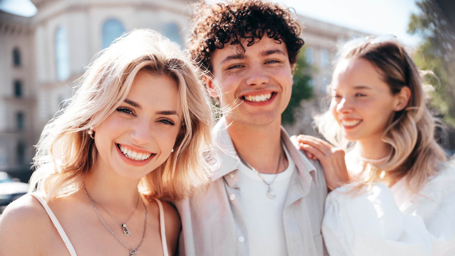 two women and a man smiling outside on a sunny day