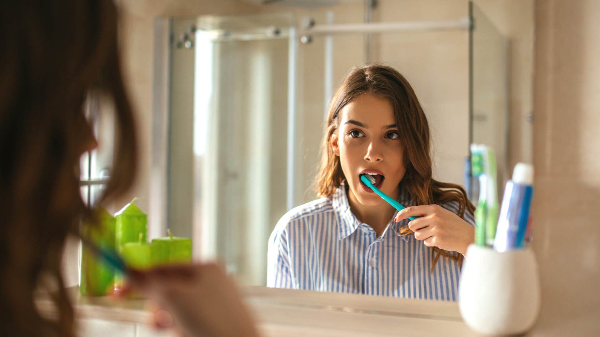 Portrait of a beautiful woman brushing teeth and looking in the mirror in the bathroom before work