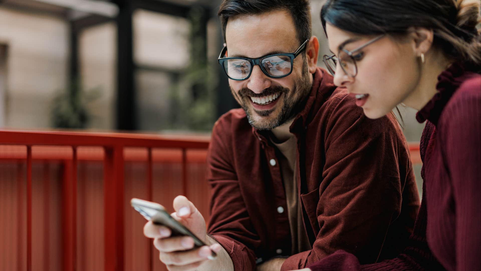 Smiling businessman holding and using a mobile phone, showing something to his female colleague