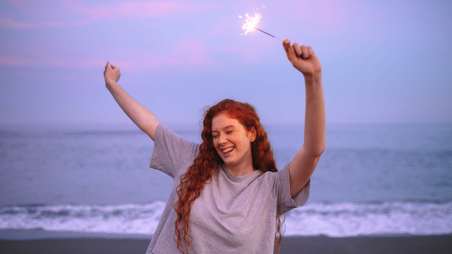 Joyful young woman celebrating with bengal lights at the beach