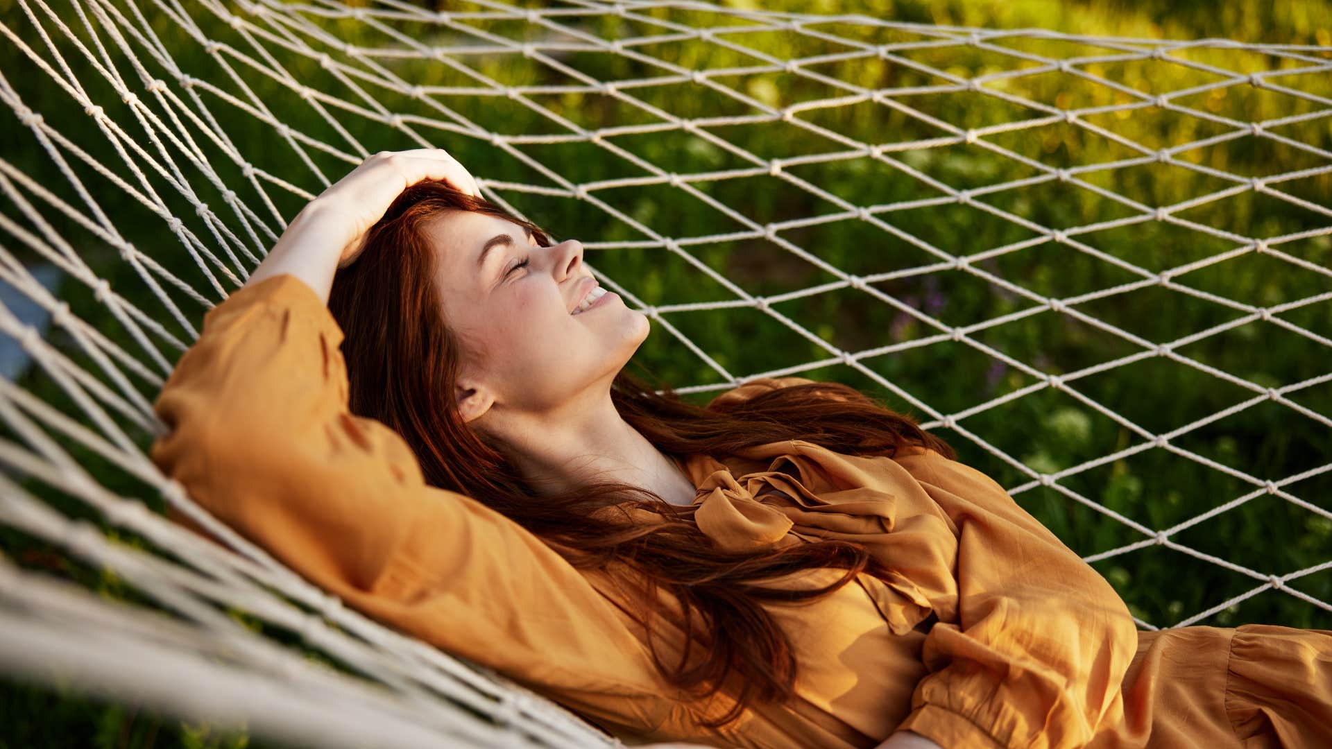 a happy woman is resting in a mesh hammock with her head resting on her hand