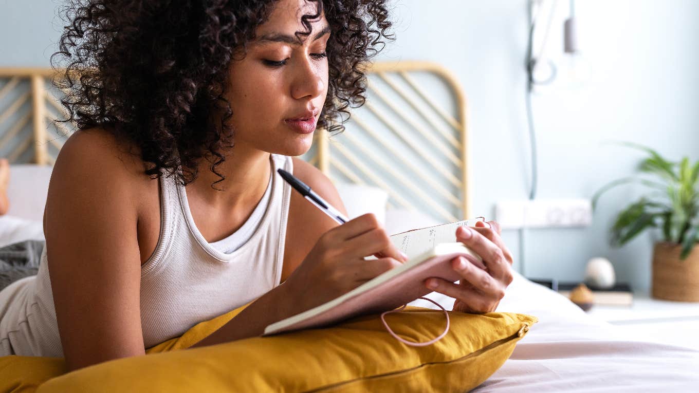 woman laying in bed writing in journal