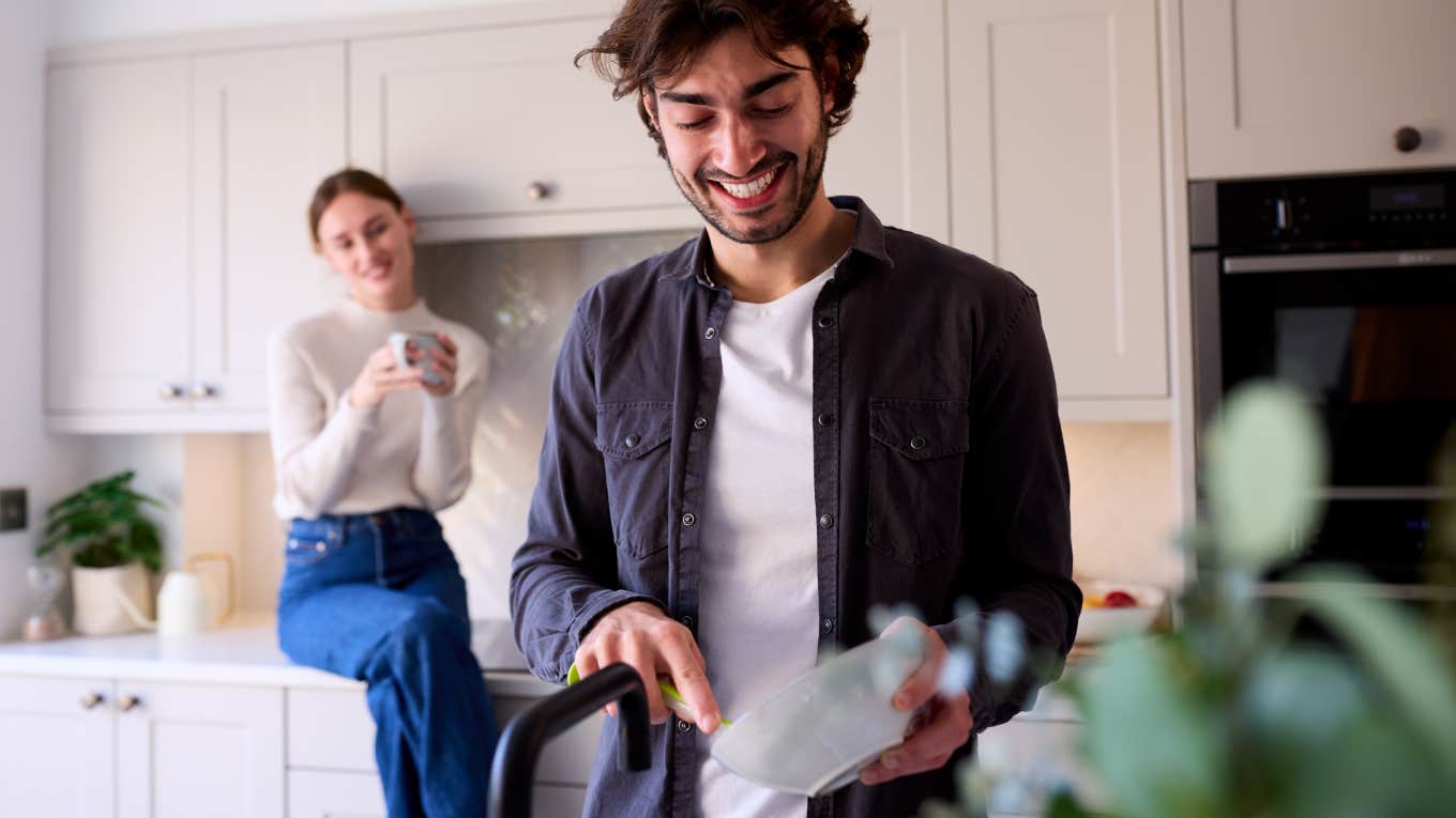 portrait of husband washing dishes and wife sitting on counter behind him