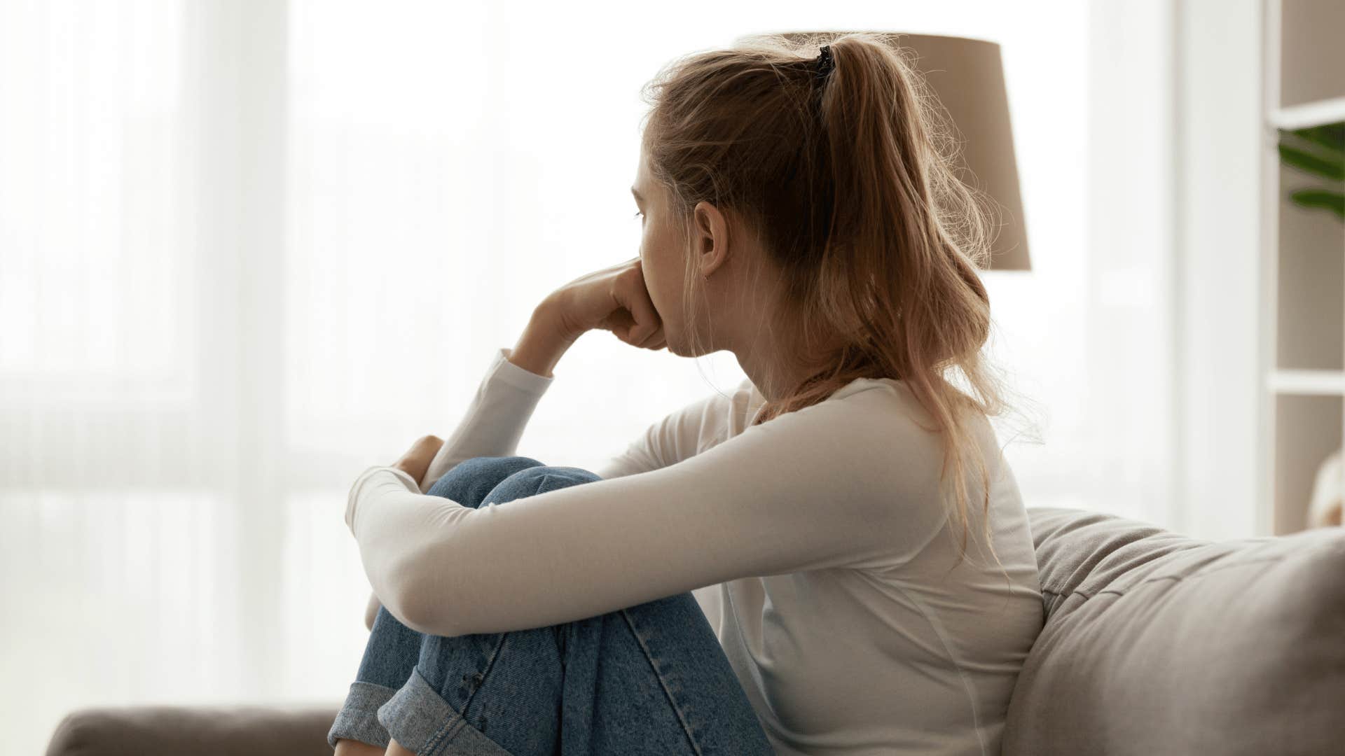 upset woman sitting on couch looking out window