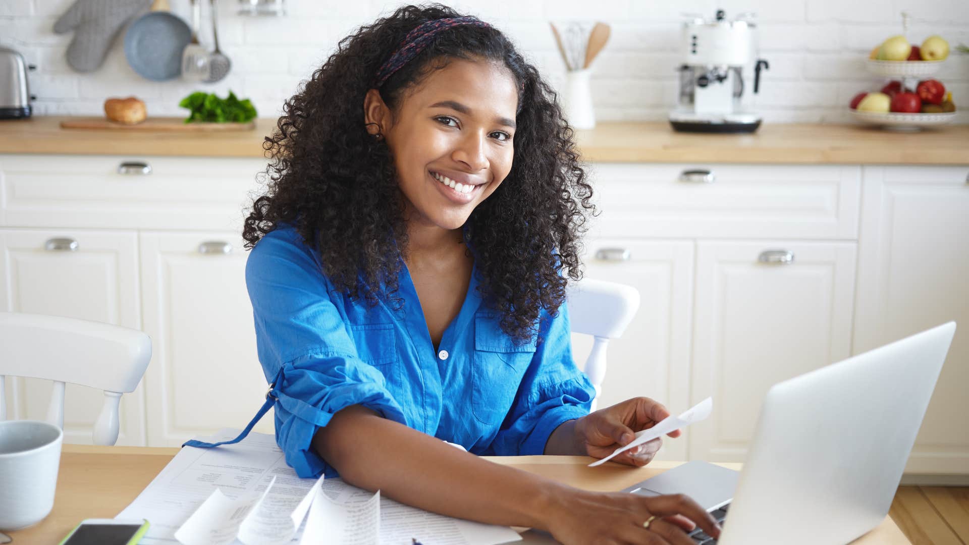 Woman smiling and doing bills on her laptop.