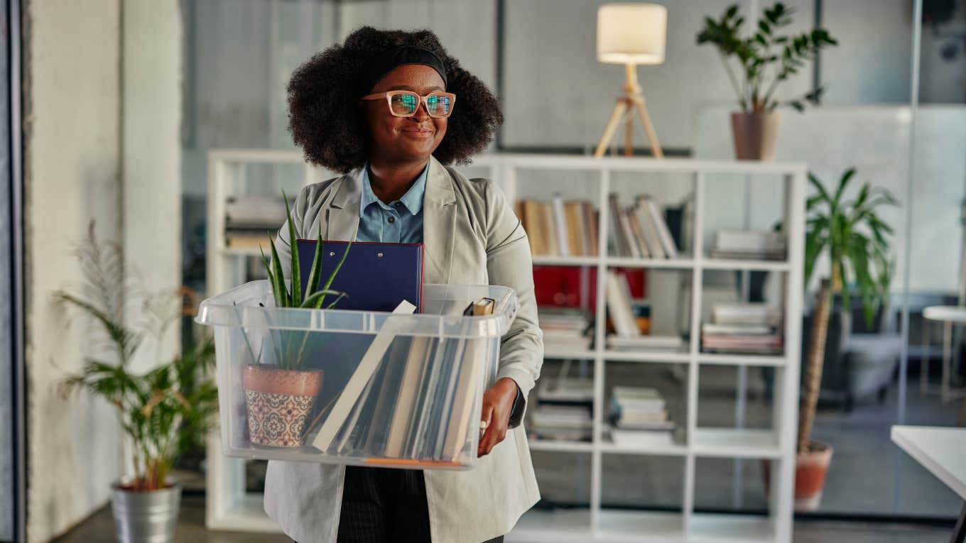 Young smiling african businesswoman entering in office and carrying box with her working supplies while going back to work