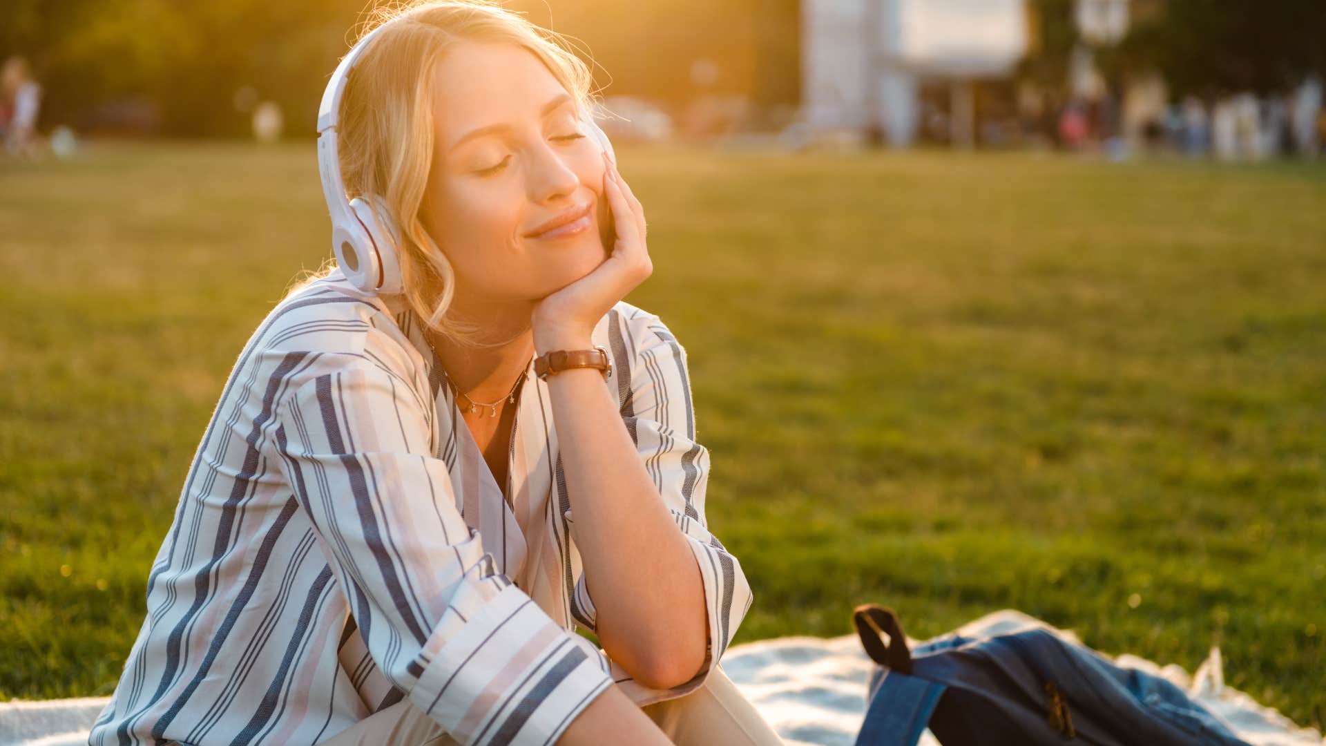 woman sitting on blanket in grass listening to music with headphones