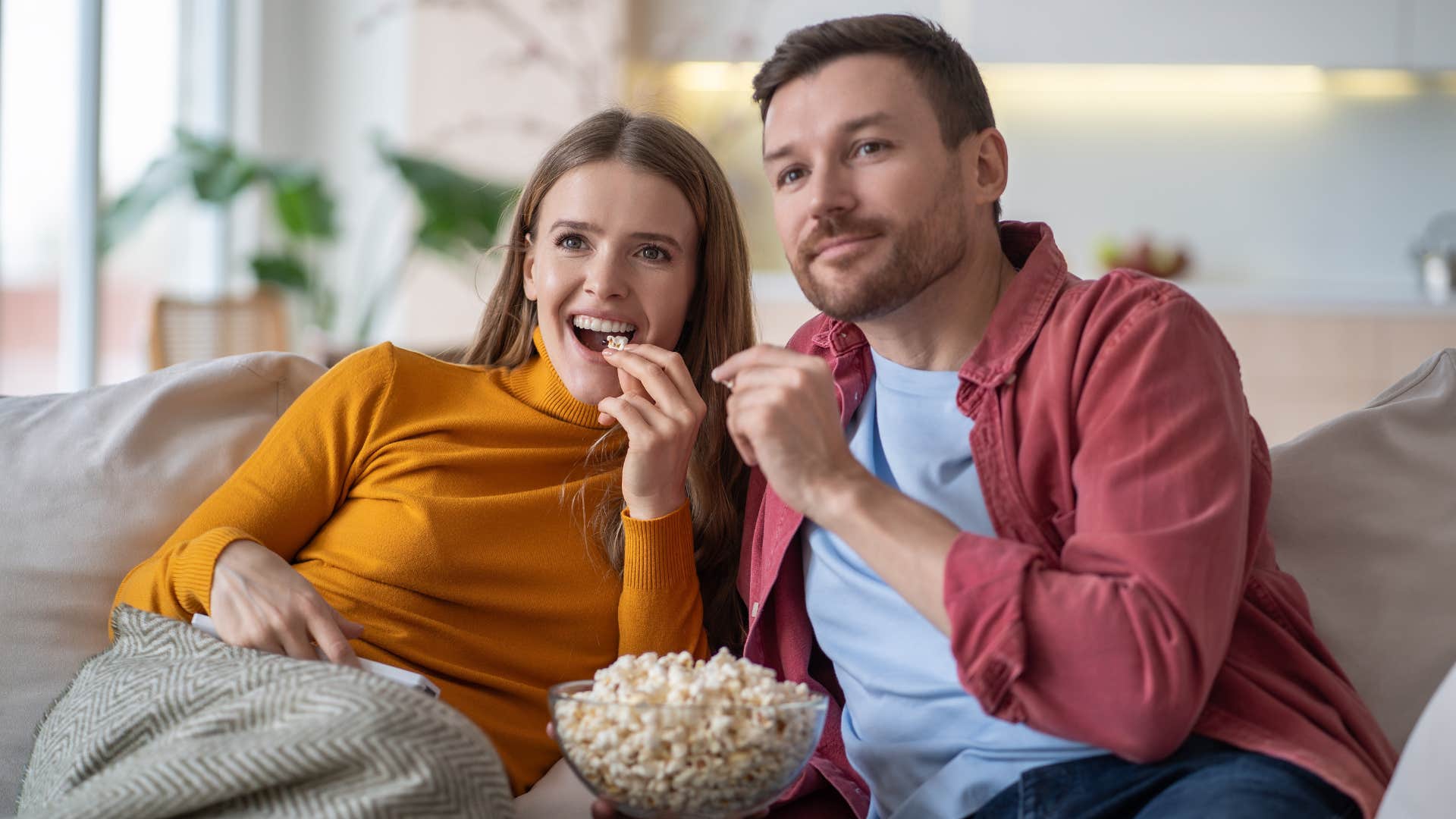 couple sitting on couch watching TV with popcorn