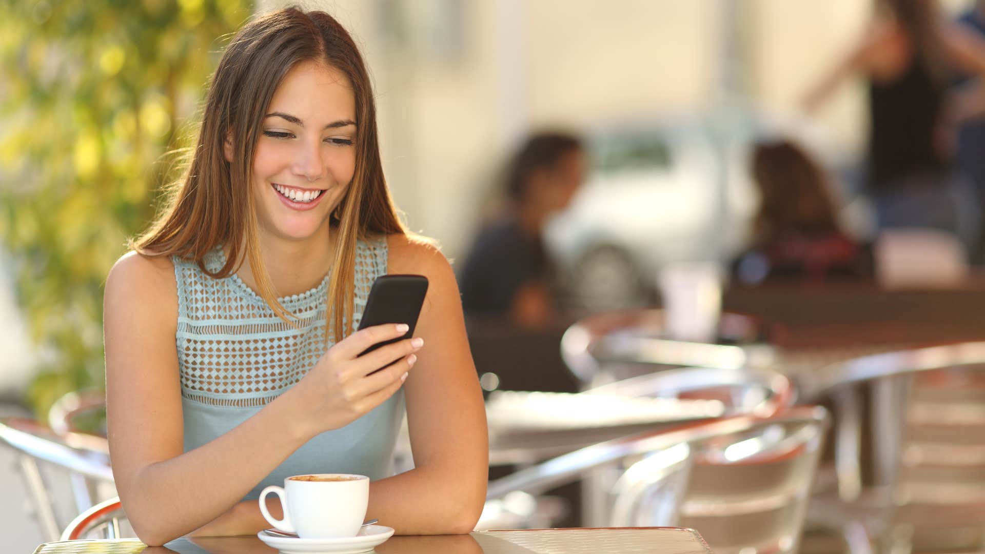 woman sitting at a cafe table texting on her phone