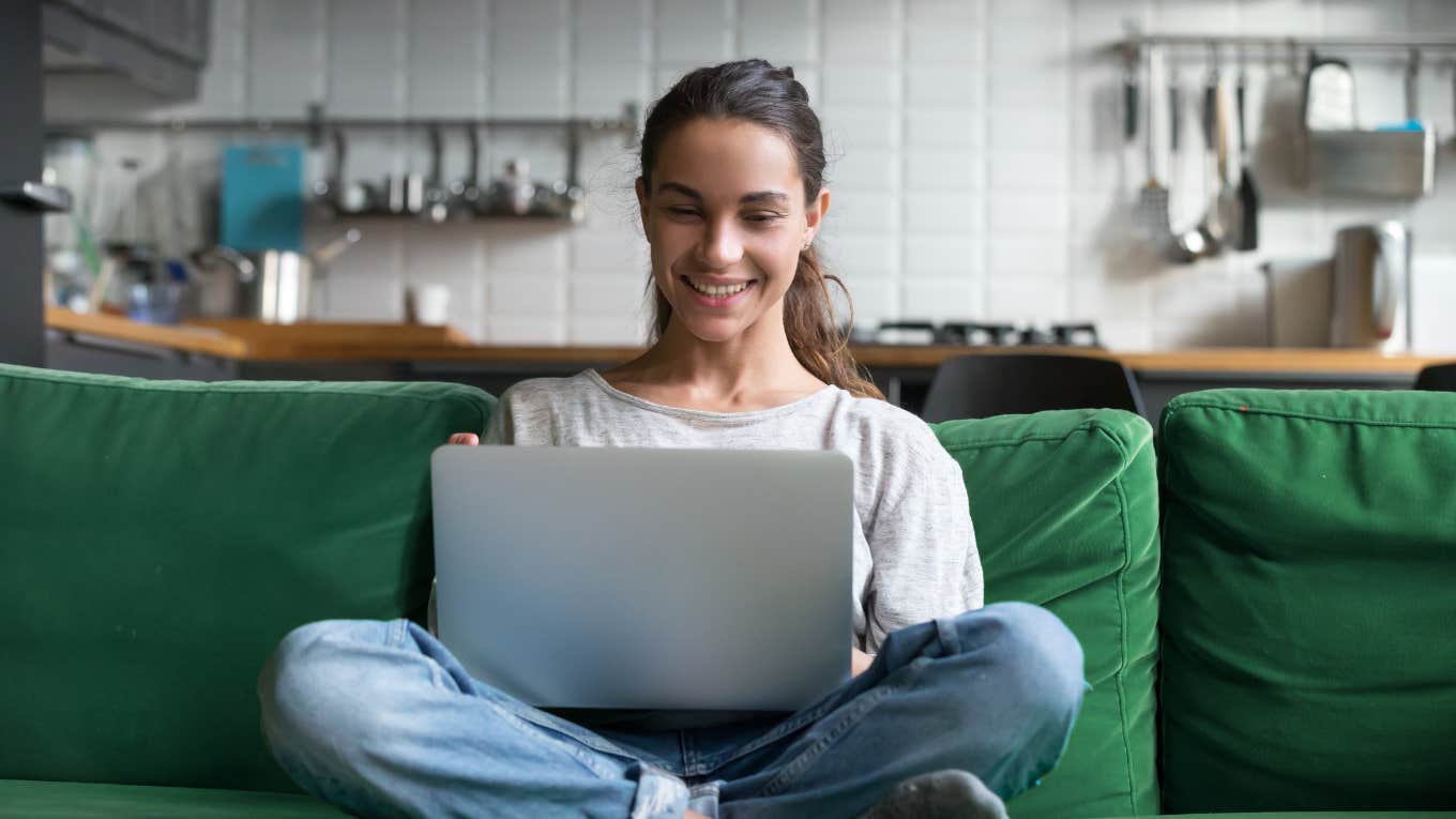 millennial smiling while looking at laptop on couch