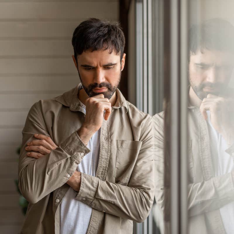 contemplative man leaning on a large window pane with his reflection visible