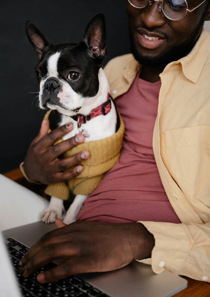 man working remotely on laptop while holding dog