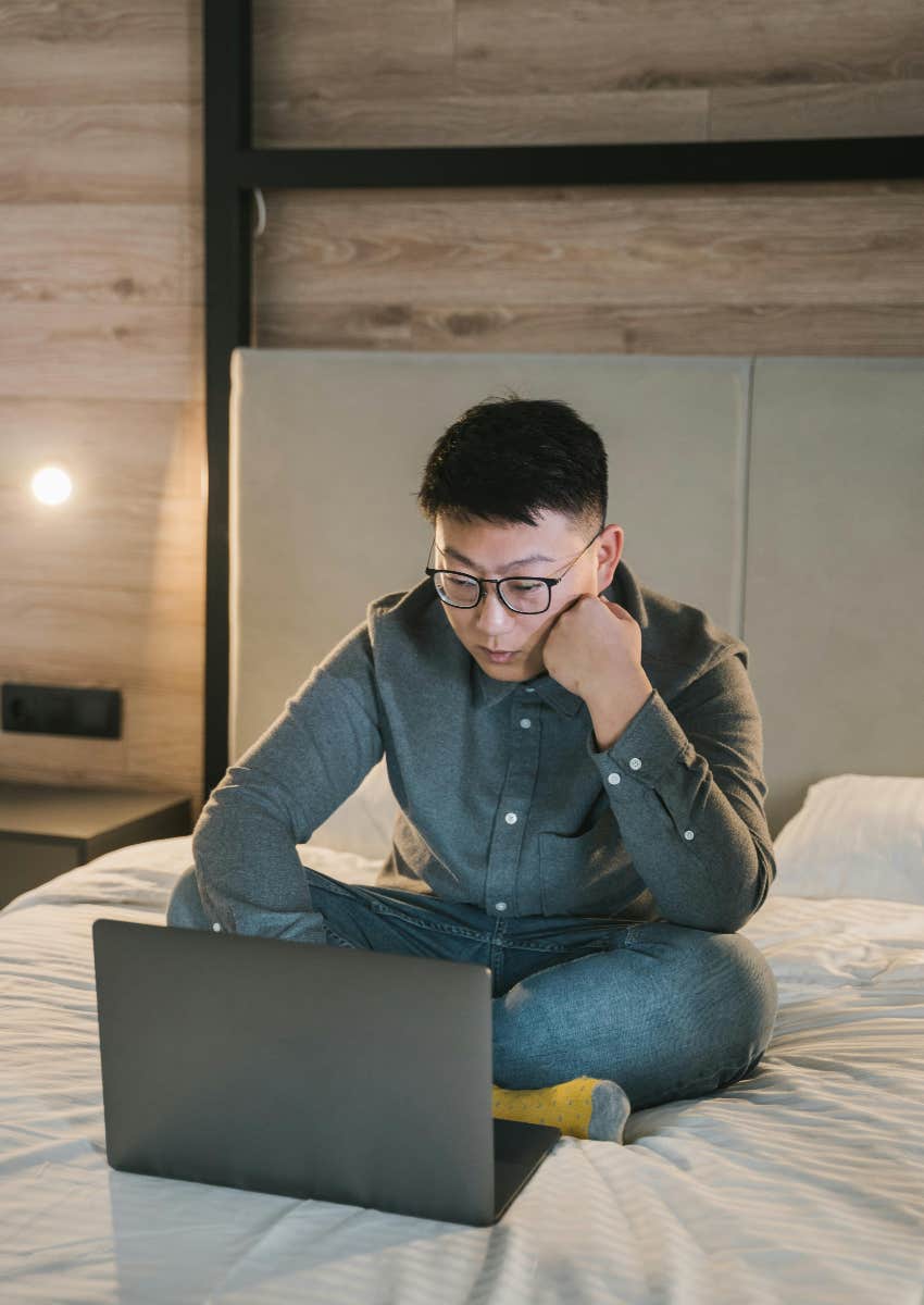 man working from home sitting on his bed with laptop