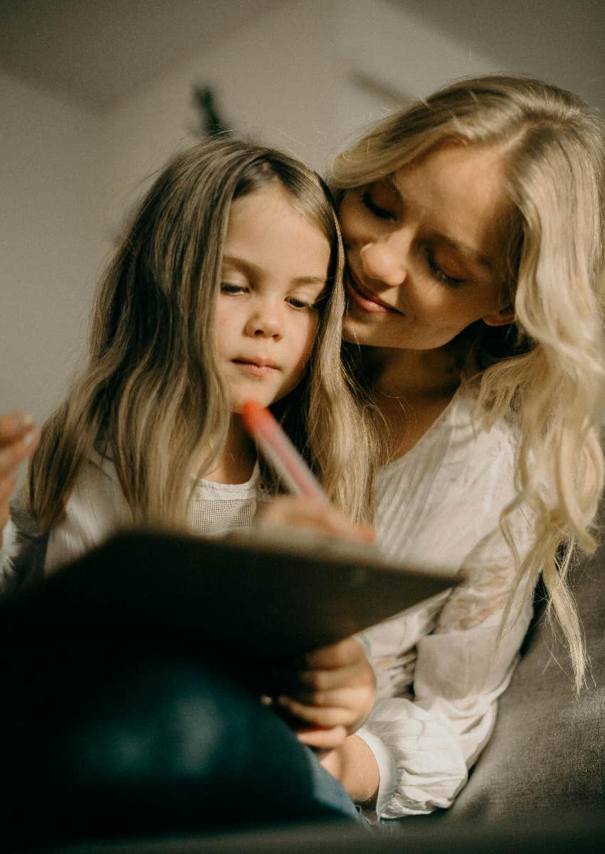 mother smiling down at her daughter while she writes