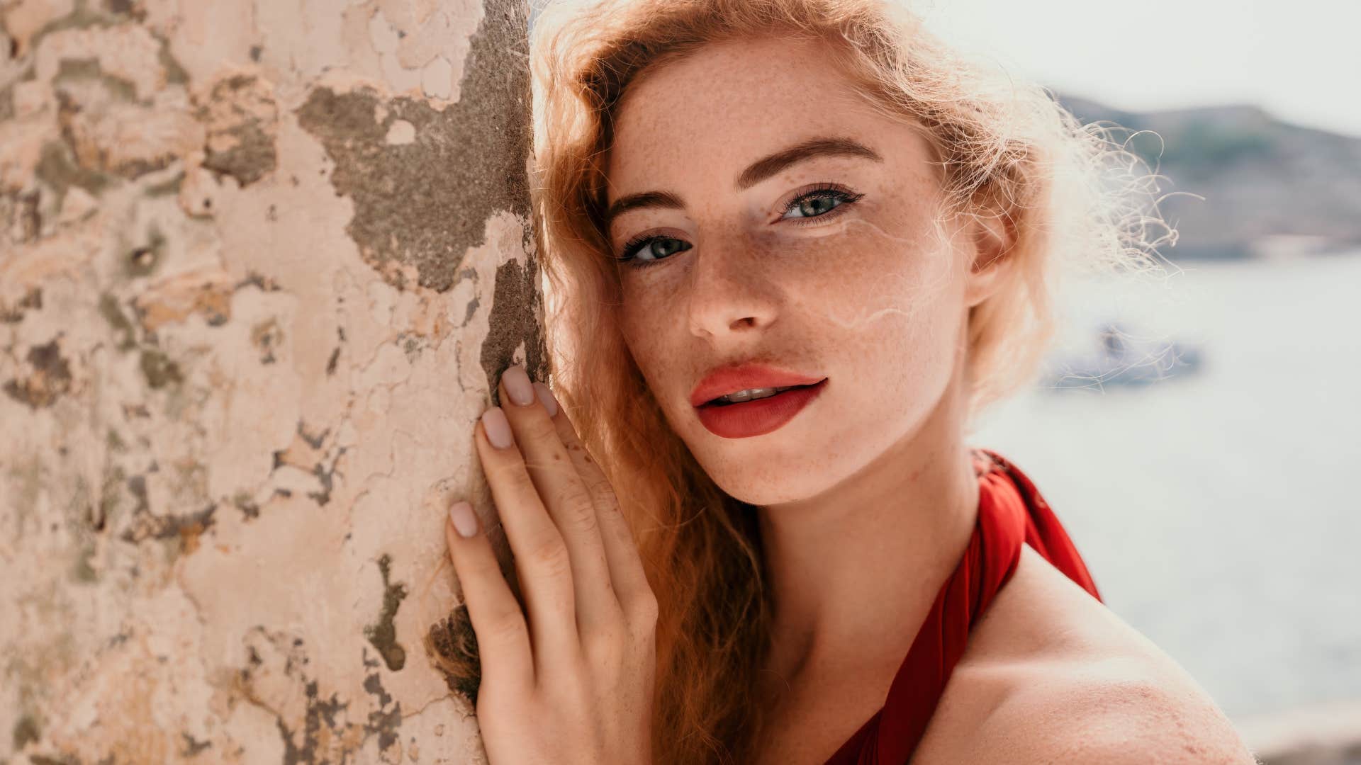 Curly redhead caucasian woman with freckles, long neck and red tank top