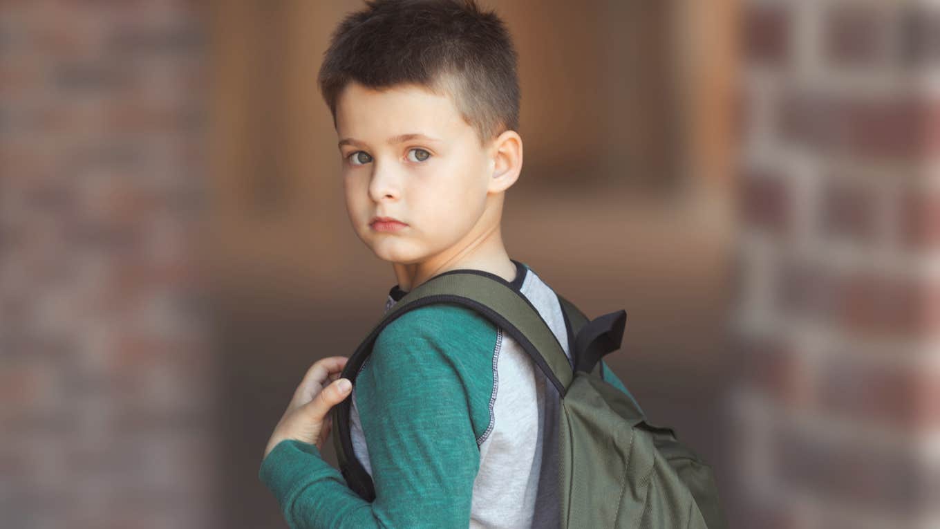 Young boy with a backpack standing in front of his school.