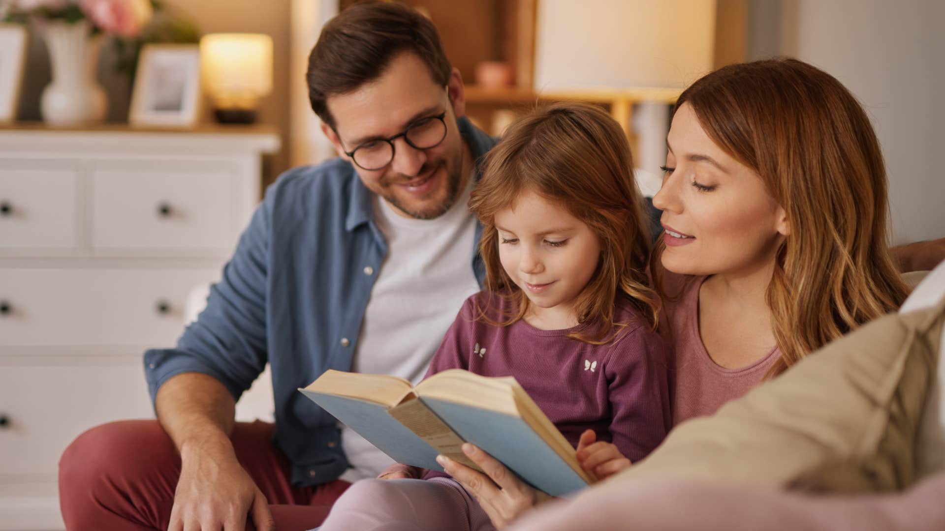 Family smiling and reading with their young daughter