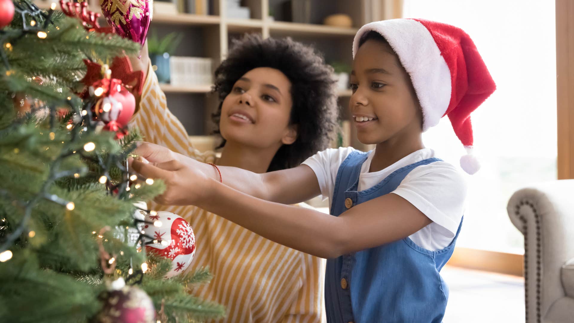 Mom smiling and decorating a Christmas tree with her daughter