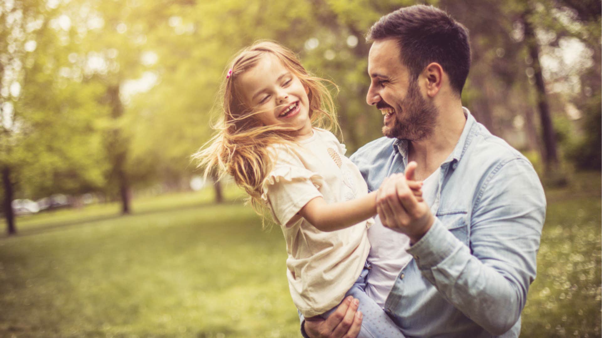 Dad smiling and dancing with his young daughter outside