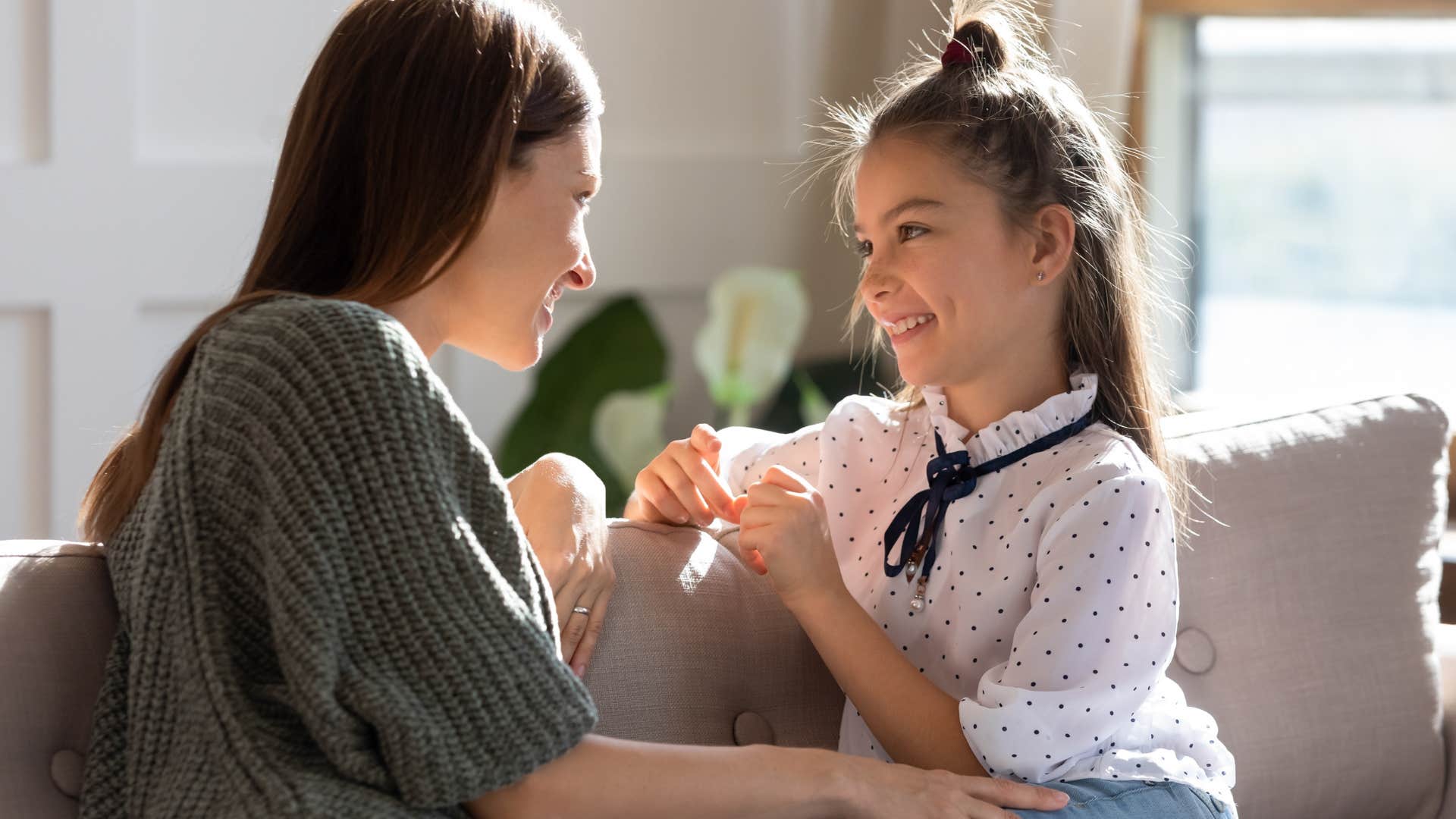 Young mom talking to her smiling daughter on the couch