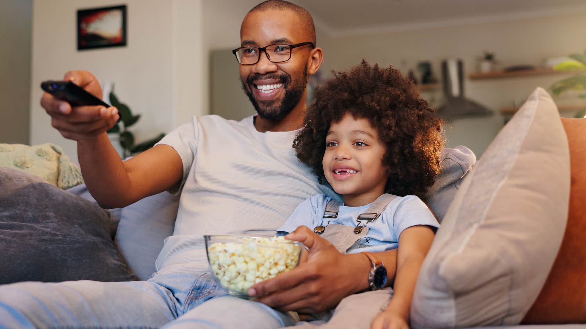 Dad smiling and watching a movie with his young son