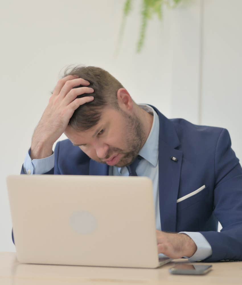 overworked man holding his head and looking at computer