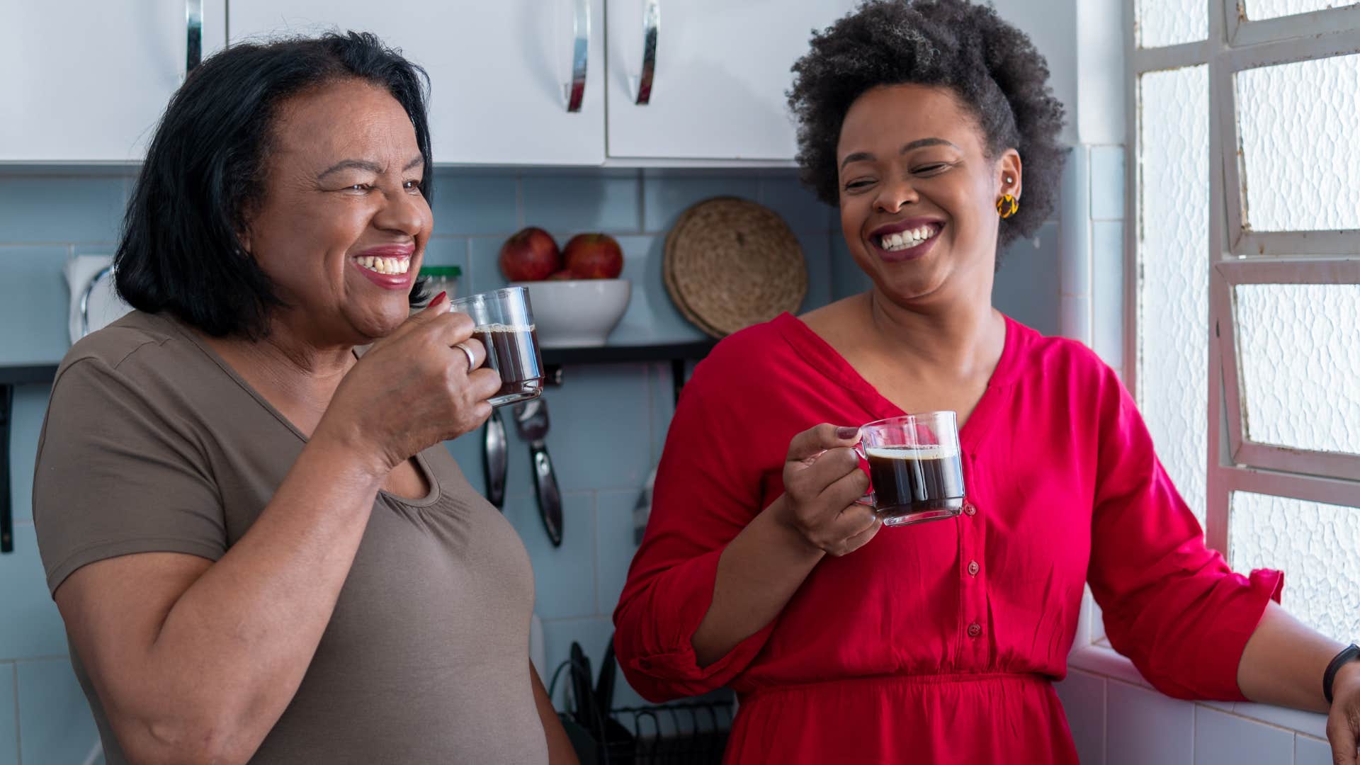 Mother and adult daughter smiling and drinking coffee together.