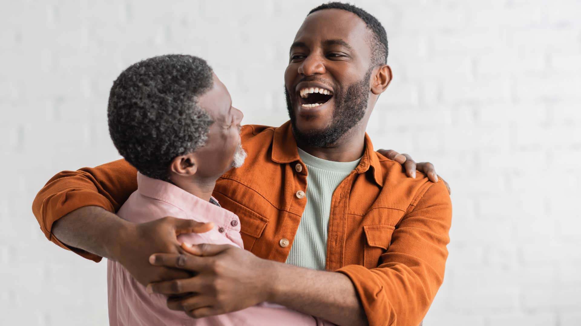 Adult son hugging his father and smiling.