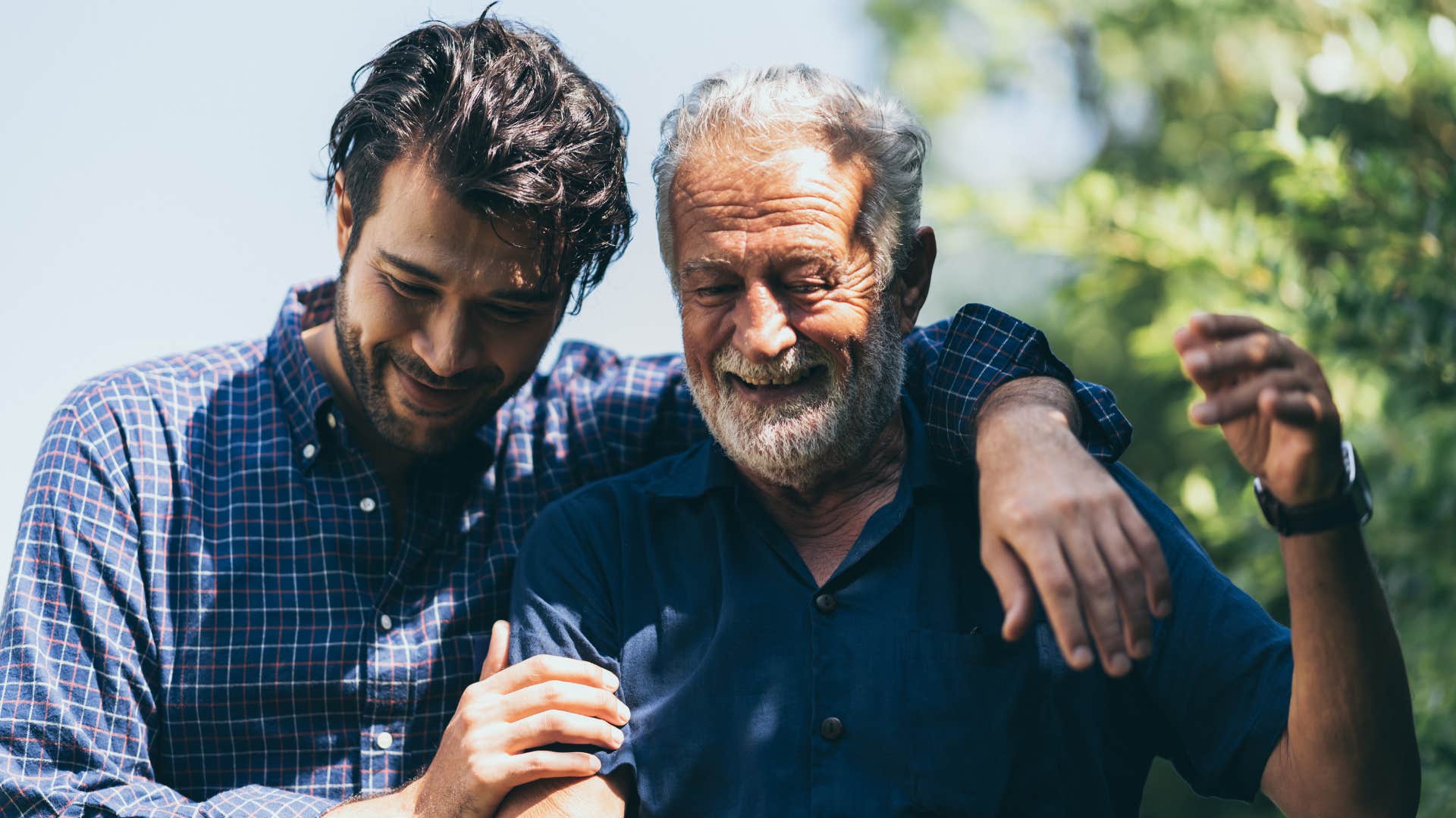 Adult son hugging his father while walking outside.