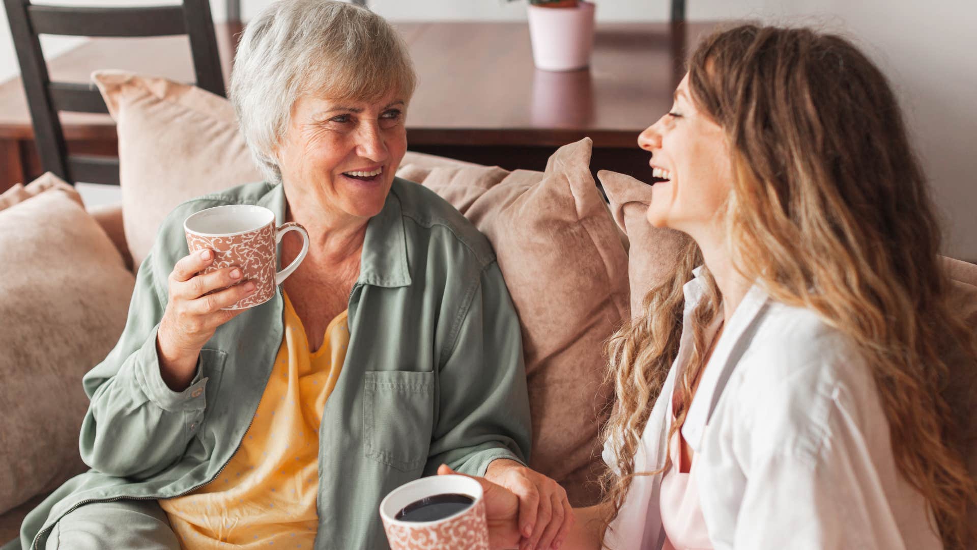 Mother and adult daughter laughing and drinking coffee together.