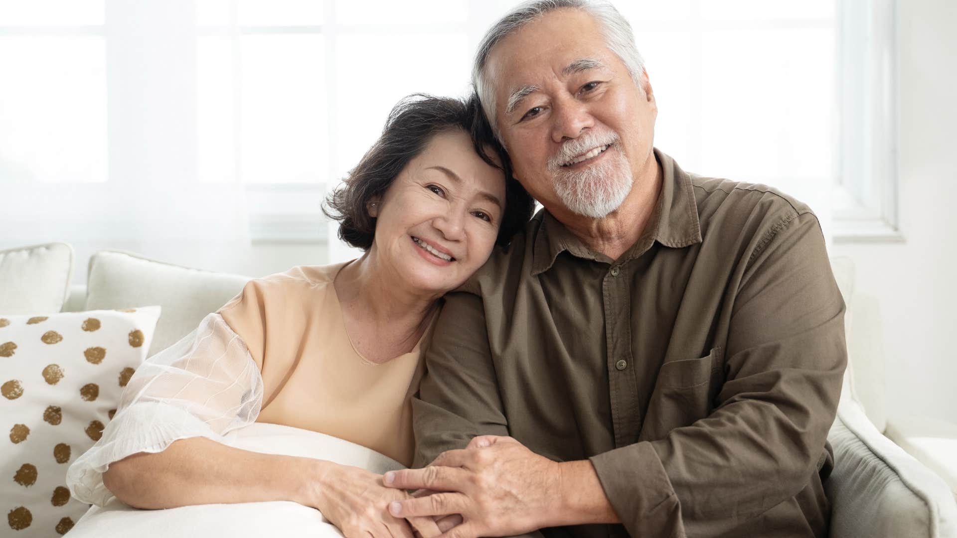 Older couple smiling and sitting on a couch together.