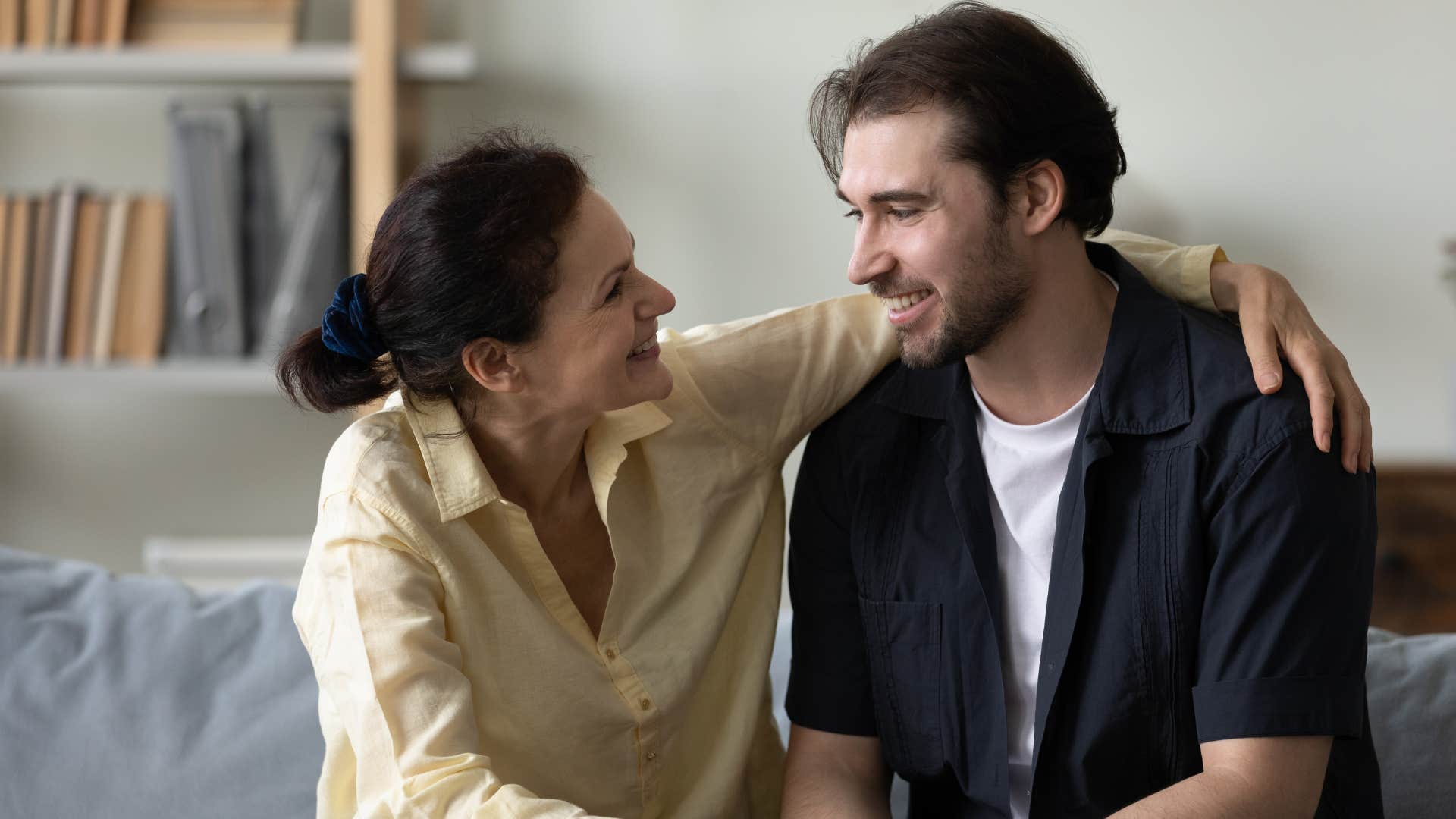 Adult son and mother smiling on the couch together.