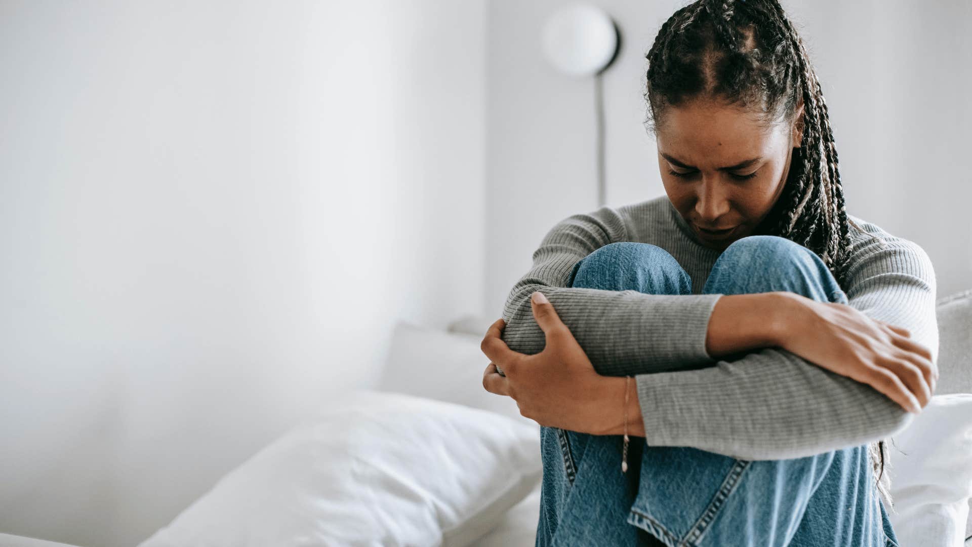 woman hugging her knees to her chest on bed