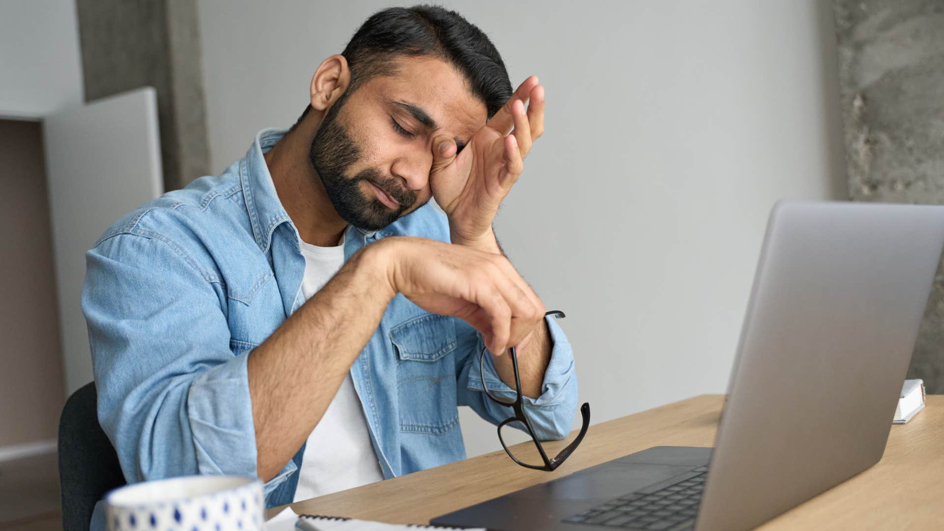 Tired man sitting in front of his laptop rubbing his eyes.