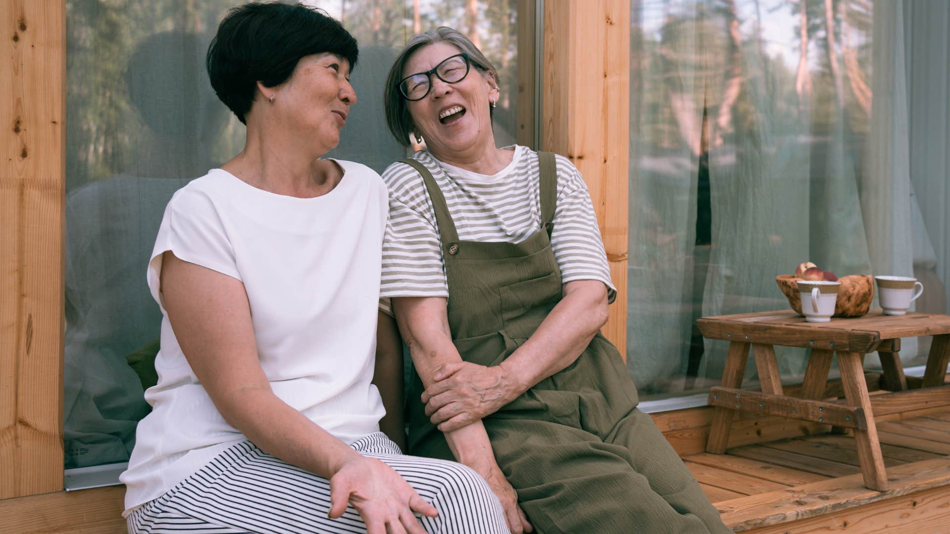 Two older women talking and laughing on a porch.