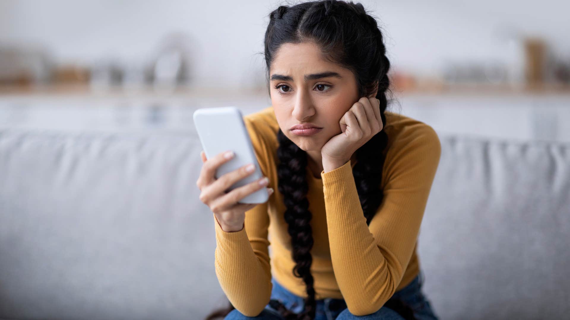 Woman looking sad staring at her phone.