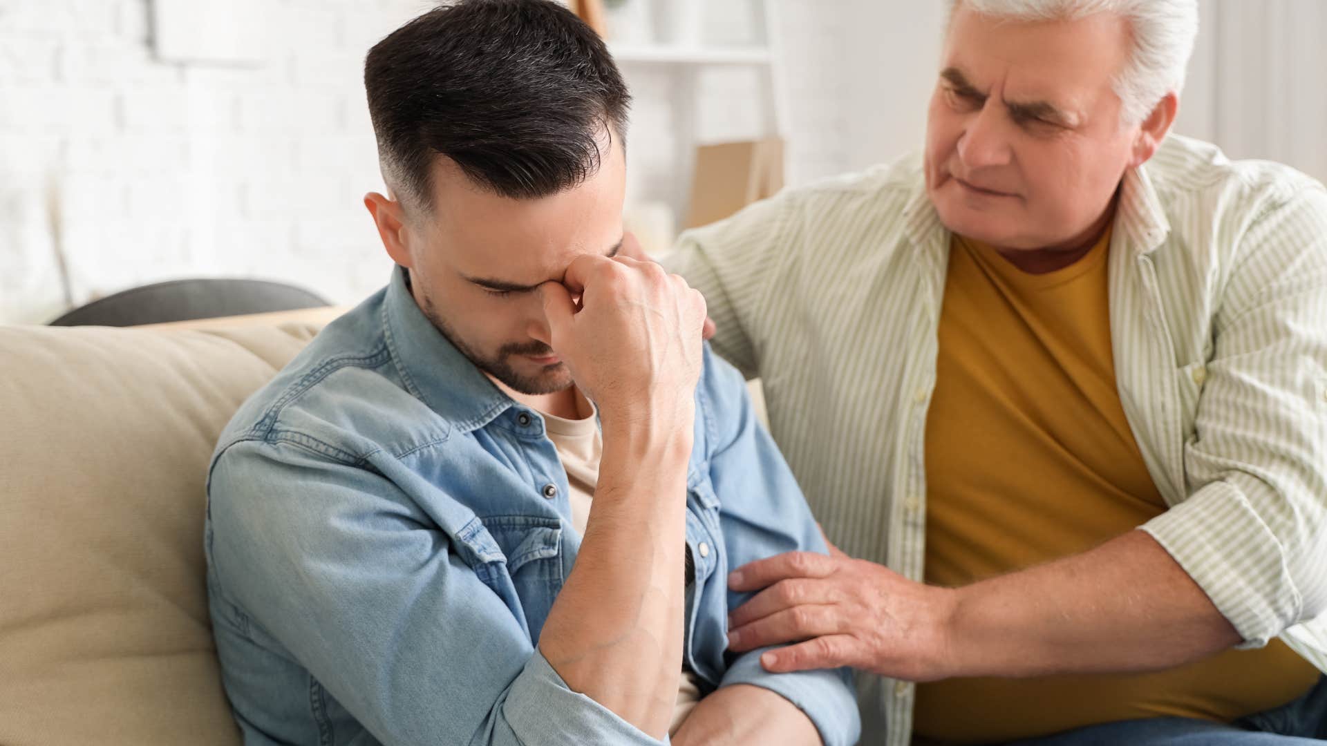 Man comforting his adult son on the couch.