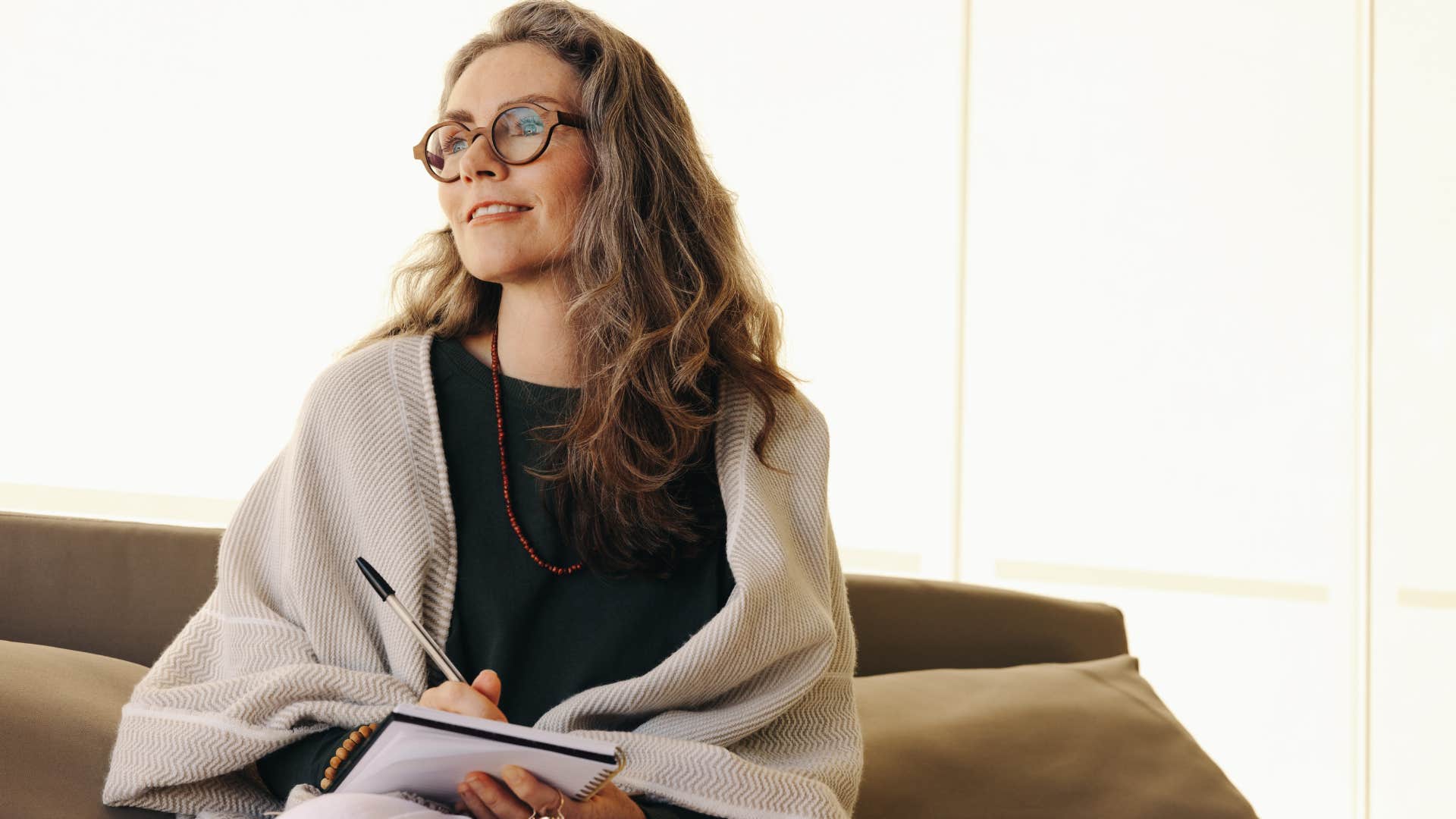 Older woman smiling while writing in her journal on the couch.