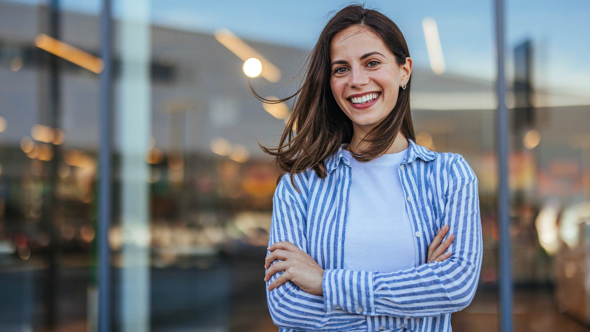 Smiling woman crossing her arms outside.