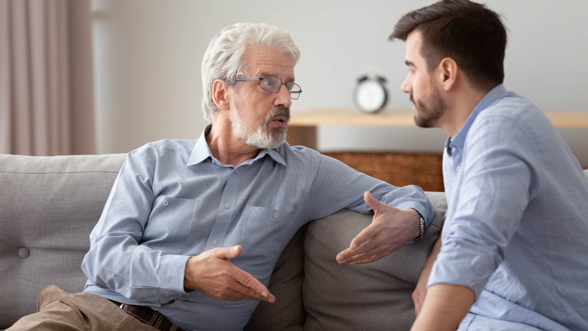 Older man arguing with his son on the couch.