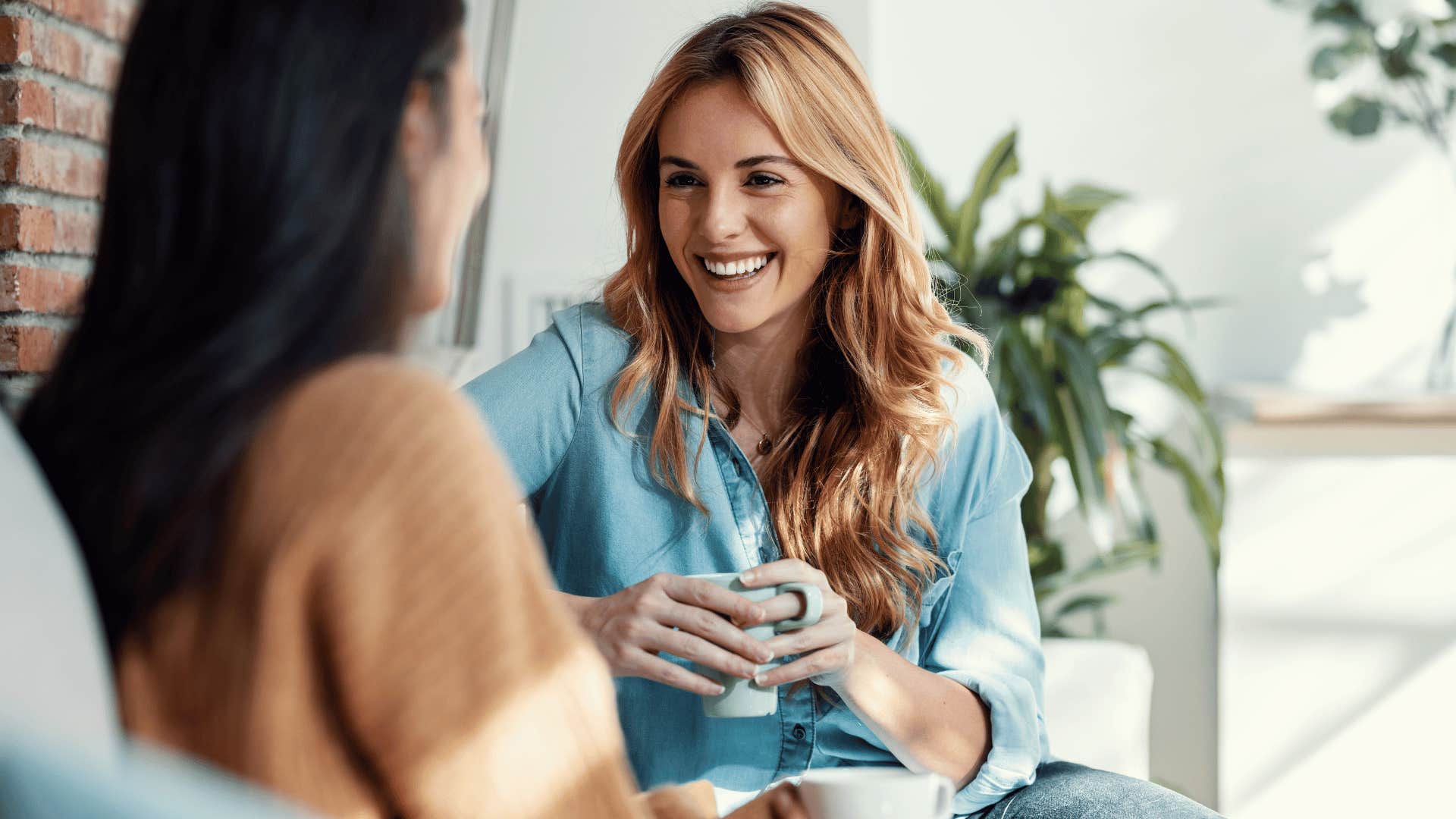 two women chatting on the couch while drinking coffee