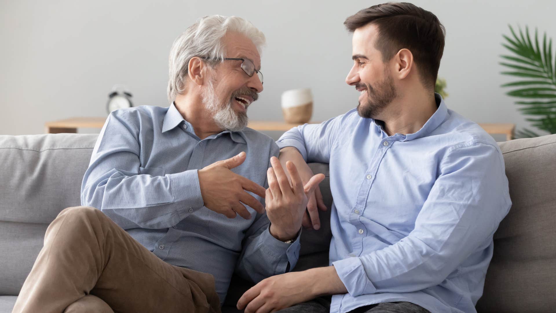 Adult son talking to his happy father on the couch